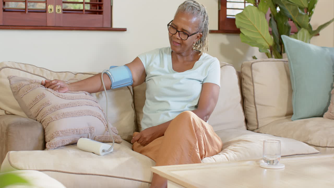 Elderly woman checking blood pressure at home, sitting on comfortable sofa