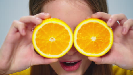 closeup cheerful woman having fun with two orange slices at camera in studio.