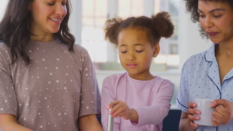 family with two mums wearing pyjamas making morning pancakes in kitchen at home with daughter