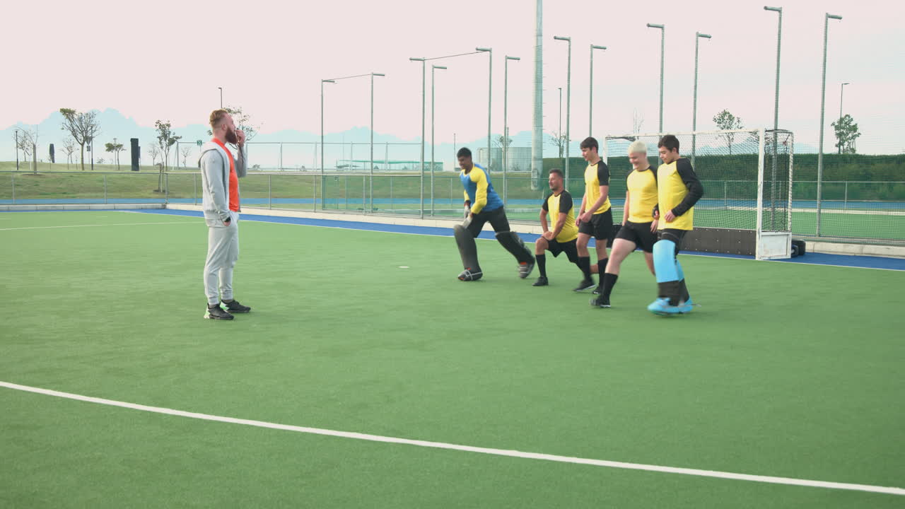 male hockey team training on field, players doing squats with coach guiding them