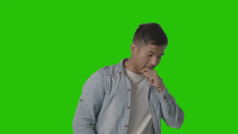 studio shot of casually dressed young man sneezing against green screen