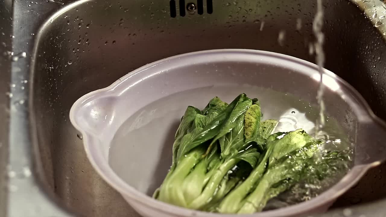 Running water filling up a bowl with wilted bok choy to be soaked and cooked to avoid food wastage, sustainable zero waste lifestyle