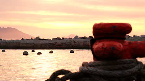 Peaceful-sunrise-view-from-behind-bollard-on-quay-of-floating-buoys-and-pier