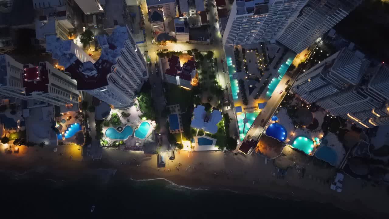 Vertical drone shot capturing Acapulco’s illuminated hotel district at night
