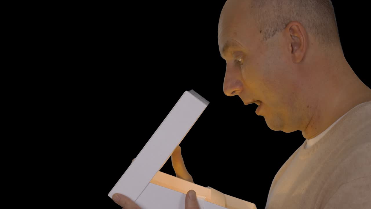 캐주얼 베이지 스웨터를 입은 성인 백인 남자가 선물 상자를 열고, 선물 상자 안을 바라보는 남자가 얼굴에 스포트 라이트를 니다.