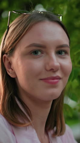 primer plano de una mujer con una sonrisa cálida, rodeada de árboles verdes y luz exterior suave, creando una atmósfera serena y positiva