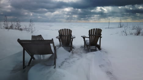 blowing snow swirls around empty cottage chairs sitting by a windy desolate lake in the canadian winter