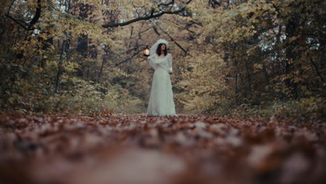 woman in white dress holding lantern in autumn forest
