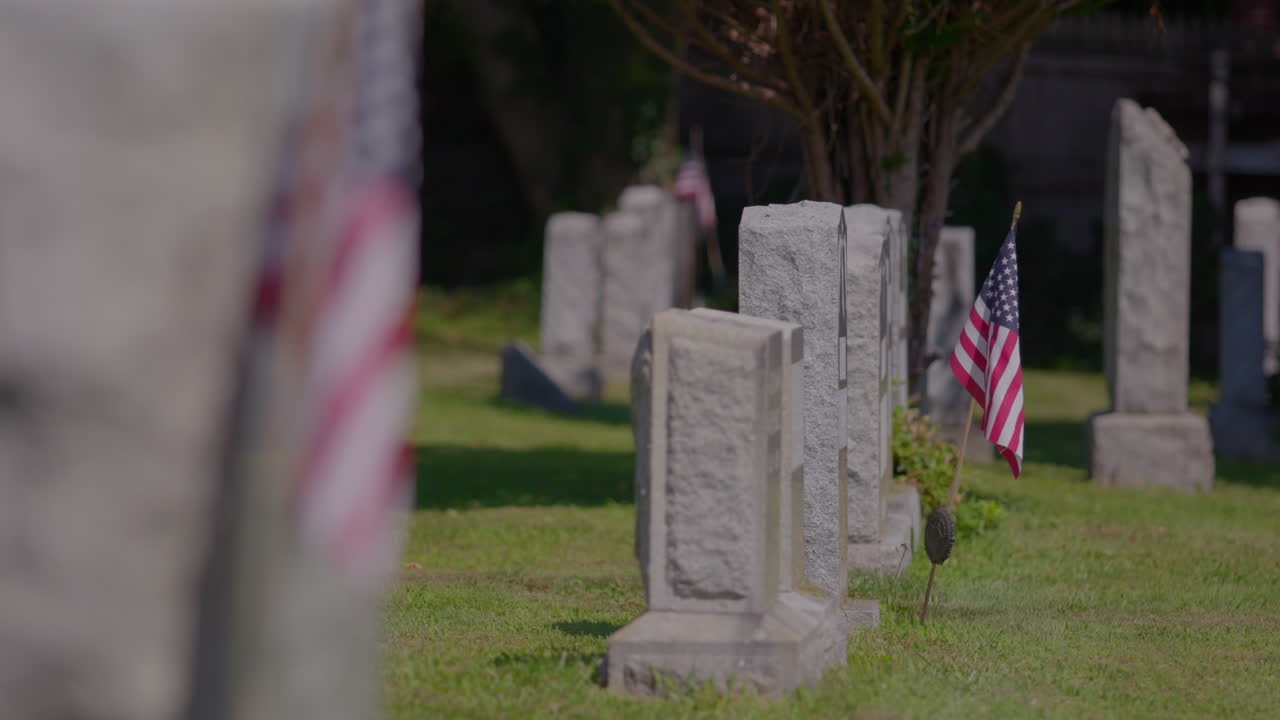 Headstones at Pelham Cemetery, The Bronx, New York. US flag beside a headstone. On a sunny day.