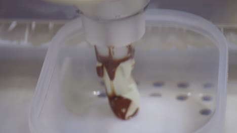 Close-shot-of-a-mechanical-arm-filling-the-freshly-made-ice-cream-in-a-pattern-in-squround-container