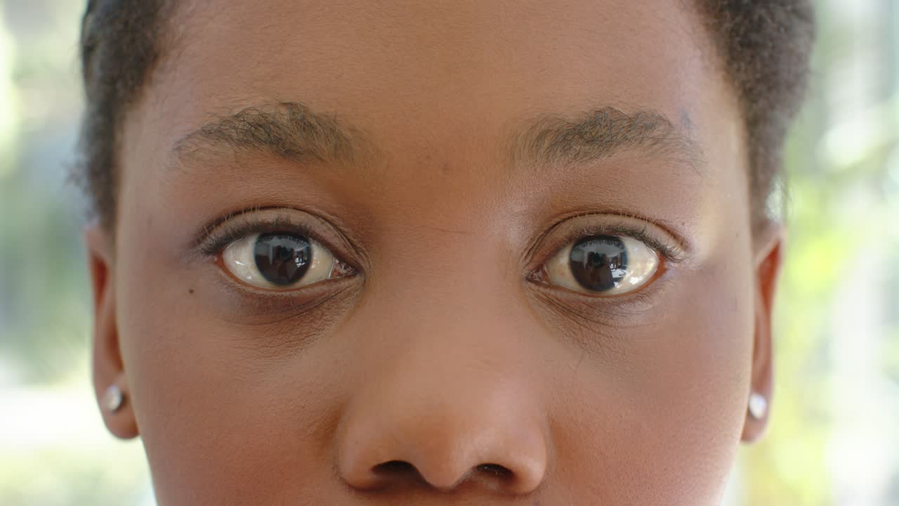 African teenage female keeping gaze with blinks wearing studs while camera recording at window