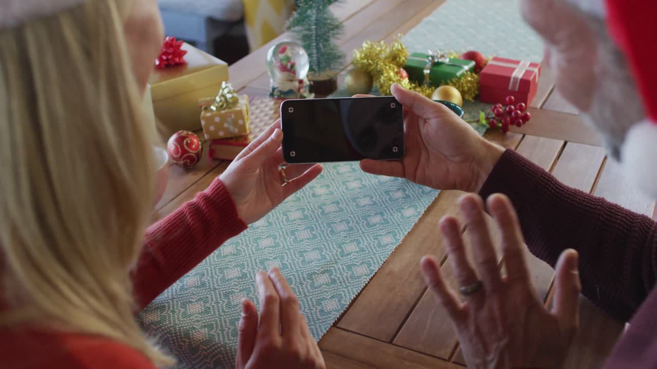 feliz pareja caucásica madura usando sombreros de santa usando un teléfono inteligente con espacio de copia