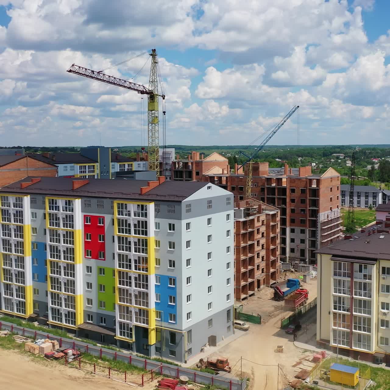 Colorful multi-storey building on a construction site. High rise buildings construction site. Big industrial tower crane with blue sky on background. Aerial drone view. City development