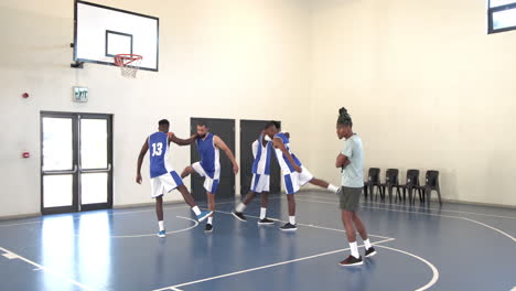 multiracial male basketball players training in pairs with coach giving instructions in gym