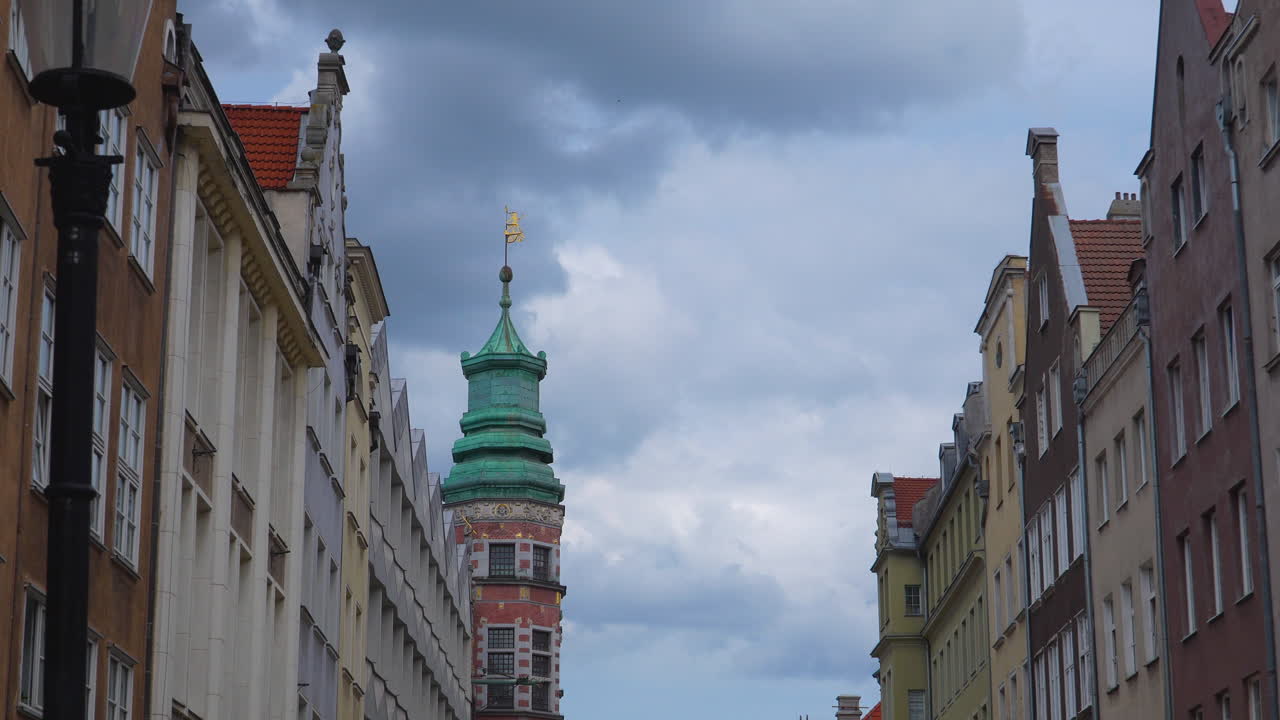 Historic tower with green copper roof and weather vane in Gdańsk under cloudy sky
