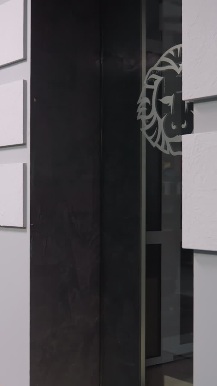 Interior of modern office with stylish design. Features office desk, white wall panels, magazine rack, and glass door with lion logo. Ideal for showcasing office space and professional environments