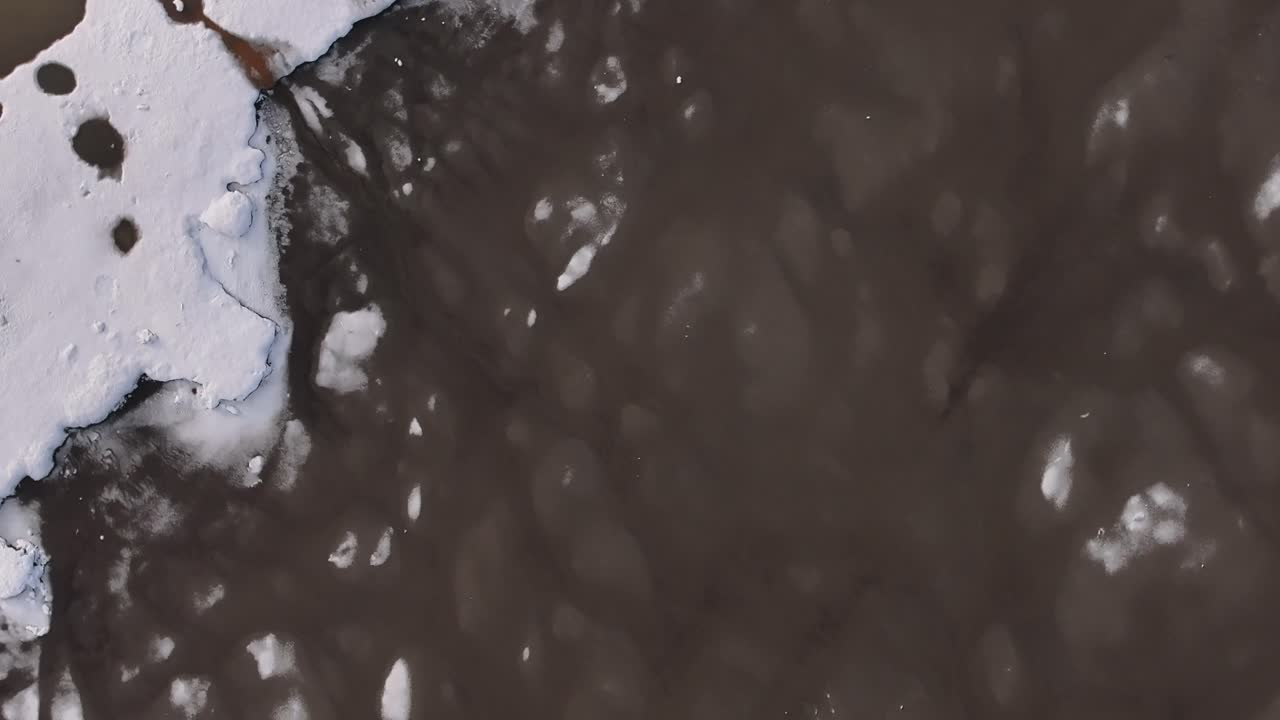 Top-down aerial view of melting snow and fragmented ice formations near Borgarfjörður Bay, Iceland, showing abstract natural patterns and thawing seasonal textures.