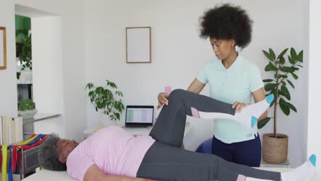 Happy-african-american-female-physiotherapist-helping-senior-female-patient-exercise-at-home