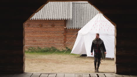 armed man in cloak walks near gate looking at territory