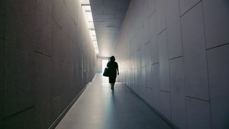 handheld, rear view of young happy attractive woman walking through perspective transit modern architect hall to bright door exit