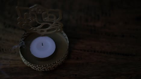 Close-up of blowing off a wax tea candle in front of Lord Ganesha golden cutout during Diwali, festival of lights, worship celebrations with smoke in dark to show the light.