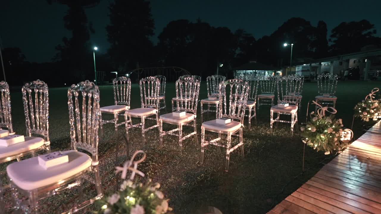 Sedie in cristallo vuote per cerimonia di matrimonio all'aperto di notte in un allestimento da giardino elegante.