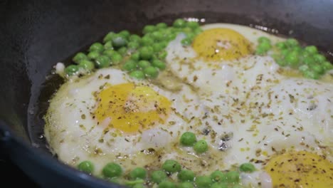 close up shot of seasoned fried eggs in olive oil and green peas