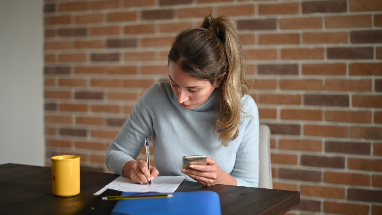 Woman working on mobile phone and writing at the office