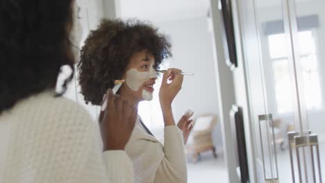 Happy-diverse-female-friends-applying-beauty-face-mask-in-bathroom