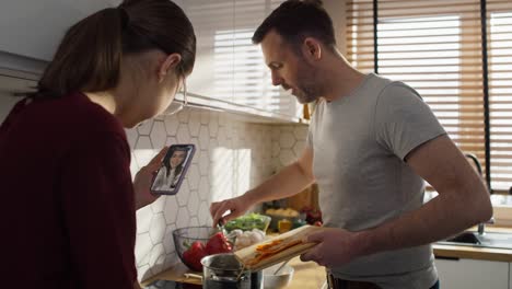 Caucasian-teenager-girl-and-her-father-having-video-call-with-mother-while-cooking