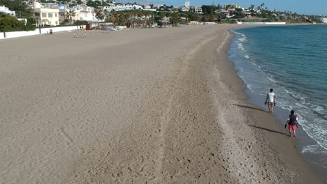 Aerial-views-over-a-beach-with-gentle-waves-and-people-walking-along-the-shore-calmly