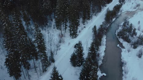 Bavarian-Austrian-alps-mountain-river-valley-with-fresh-water-at-Sylvensteinspeicher-with-a-Porsche-car-by-sunset,-winter-snow-riverbed,-trees-and-forest-and-mountains