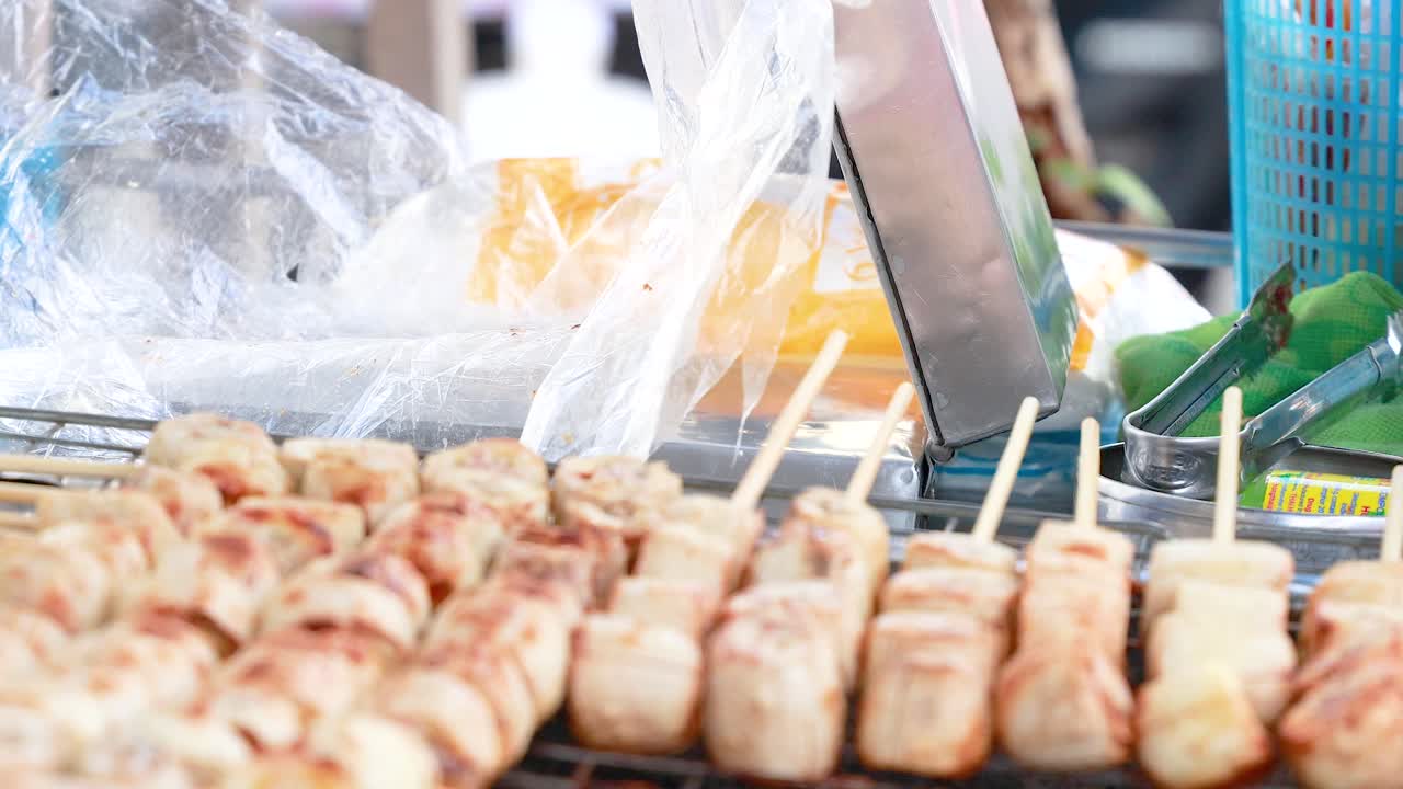 A vendor skillfully prepares grilled banana snacks on skewers at a bustling street market in Phuket, Thailand