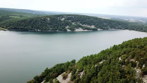 Aerial-view-of-tranquil-Devil's-Lake-in-Wisconsin,-surrounded-by-lush-forests-and-rocky-hills-under-a-cloudy-sky