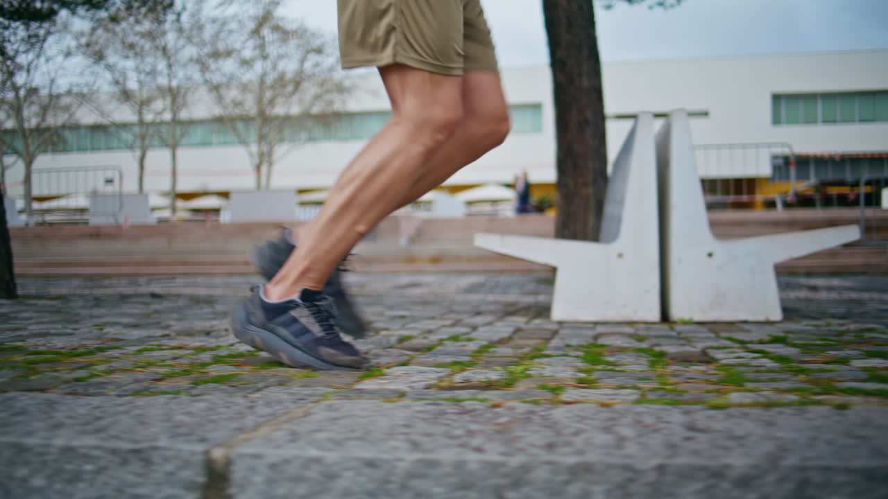 Sporty legs start running in urban park closeup. Fit male athlete workout cardio