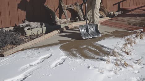 Man-shoveling-the-snow-off-of-a-sunny-walkway-in-a-suburb-in-the-mountains-of-Colorado,-USA