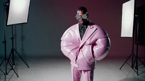 stylish male model showcasing a voluminous pink puffer jacket and matching trousers in a studio setting, illuminated by professional lighting equipment