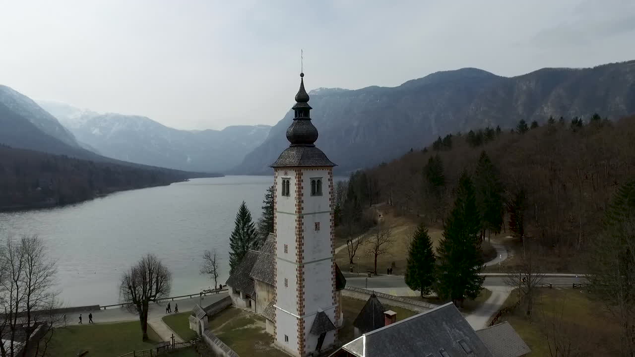 Drone che si alza in alto sopra un ponte e una chiesa dal lago di Bohinj, Slovenia