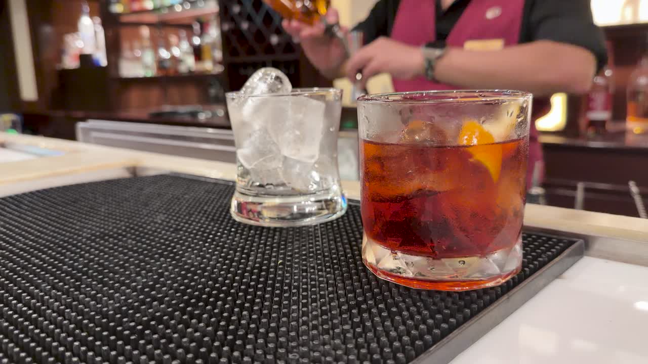 Bartender in uniform mixes classic cocktails on bar mat under warm, ambient lighting, slow motion