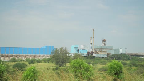 static shot of heavy loaded trucks and car crossing each other on both side of the road with an industrial plant in the background