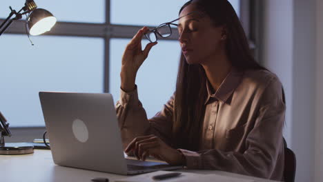 Müde-Geschäftsfrau,-Die-Spät-Am-Schreibtisch-Im-Büro-Arbeitet-Und-Einen-Laptop-Benutzt,-Nimmt-Ihre-Brille-Ab