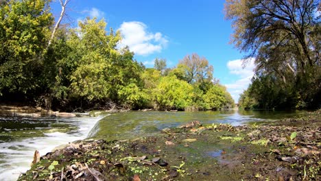 zooming past section of fallen leaves - algae, towards side view of large expanse of creek - waterfall