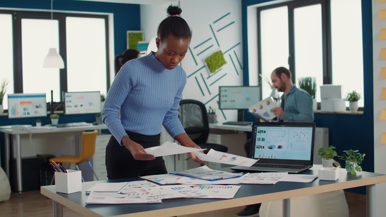African american startup employee looking at business papers with data charts comparing two sheets with statistics