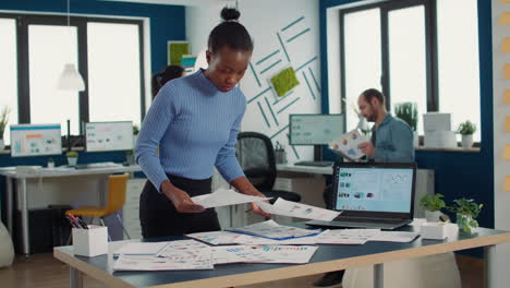 African-american-startup-employee-looking-at-business-papers-with-data-charts-comparing-two-sheets-with-statistics