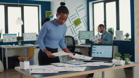 african american startup employee looking at business papers with data charts comparing two sheets with statistics