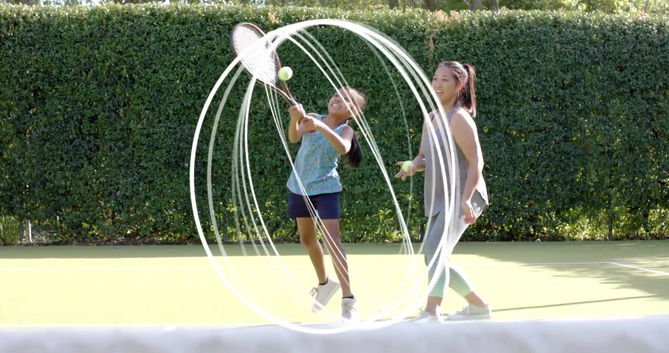 Adult woman coaching girl on tennis court, fixing grip, feeding ball, swirl tracing swing past net