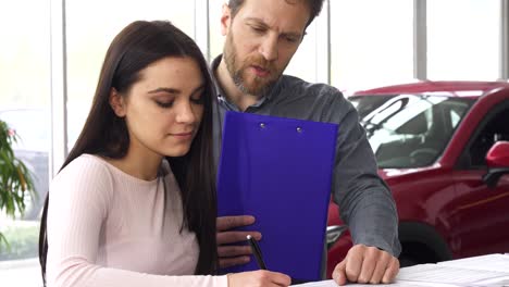 un concesionario de coches maduro firmando papeles con su cliente mujer