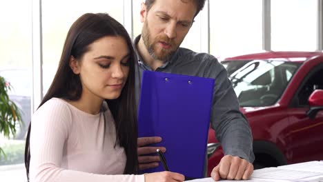 mature car dealer signing papers with his female customer