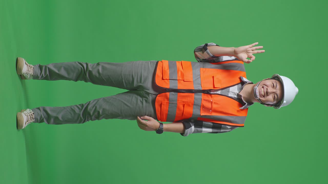 Full Body Of Asian Male Engineer With Safety Helmet Smiling And Showing Okay Gesture To The Camera While Standing In The Green Screen Background Studio