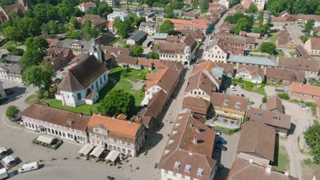 Aerial-establishing-view-of-Kuldiga-Old-Town-,-houses-with-red-roof-tiles,-sunny-summer-day,-travel-destination,-wide-orbiting-drone-shot-moving-left
